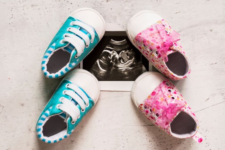 Blue and pink baby booties next to ultrasound photos at 20 weeks of pregnancy