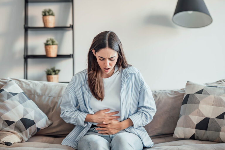 Woman suffering from stomach ache at home, holding and massaging her abdomen